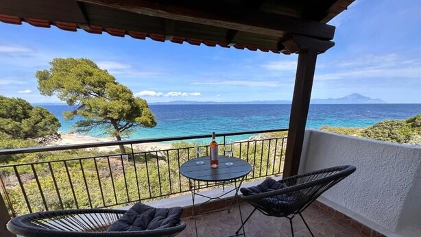 A balcony with two chairs and a table, overlooking a beach and the sea.