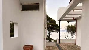 A white building with a stone pathway leading to a covered area with a view of the sea.