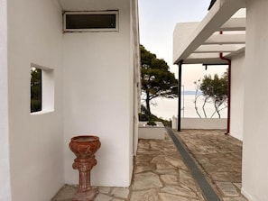 Ein weißes Gebäude mit einem steinernen Weg, der zu einem überdachten Bereich mit Blick aufs Meer führt.