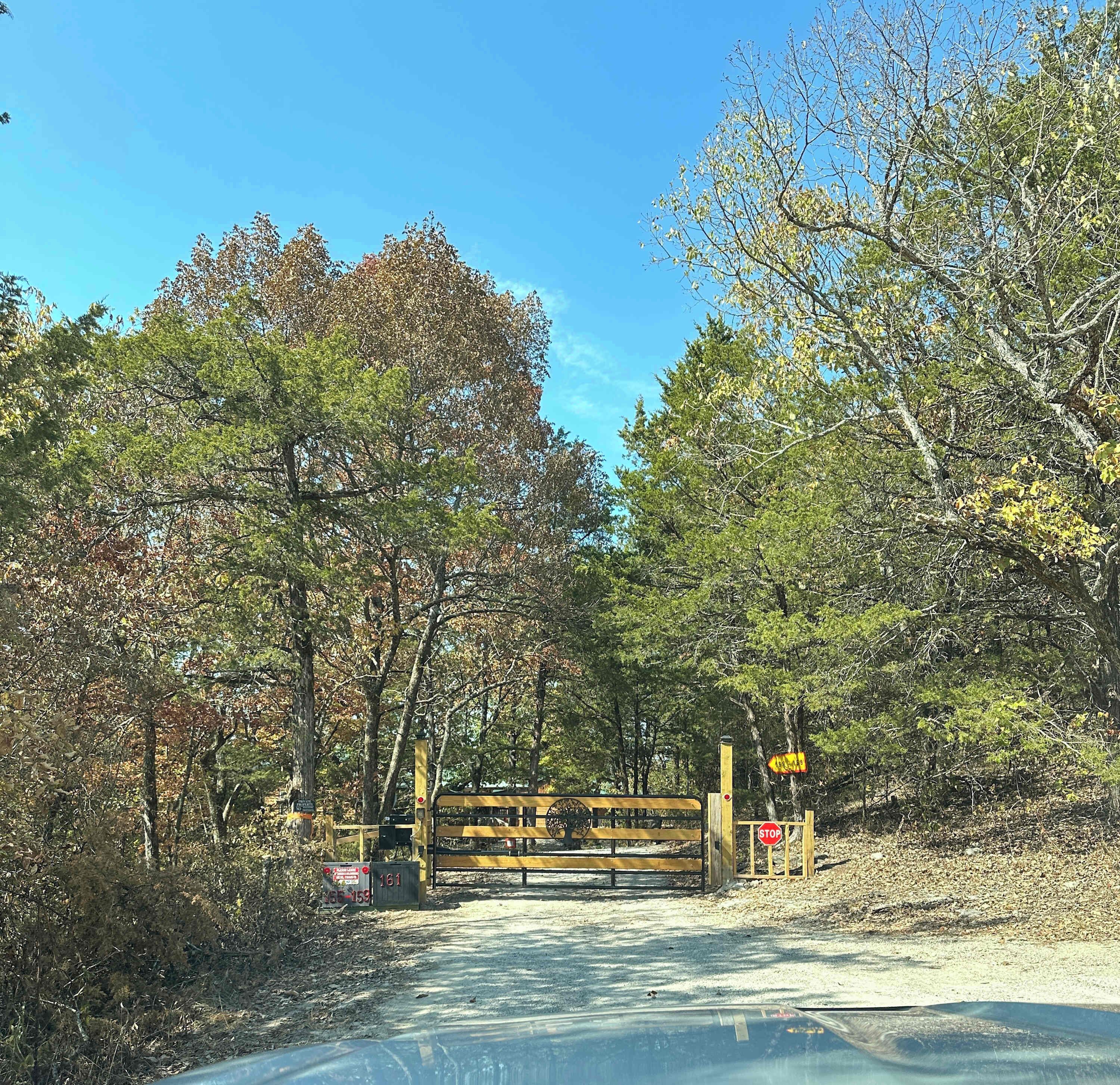 A road leading through a wooded area with a wooden gate and a stop sign.