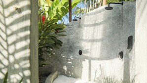 Eine Betonbadewanne mit Duschkopf, umgeben von viel Grün.