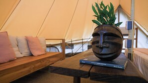 Ein Zeltinnenraum mit einer hölzernen Sitzbank, Kissen, einem Tisch mit einem Buch und einer Pflanze.
