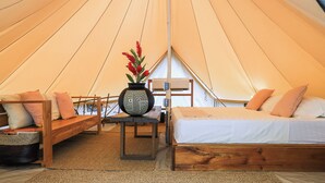 Ein Zelt mit Bett, einer Bank, einem Tisch und einer Vase mit Blumen.