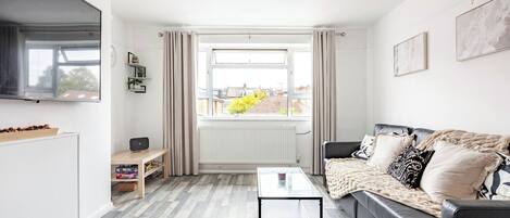 A modern living room with a sofa, a coffee table, a TV, and a window with curtains.