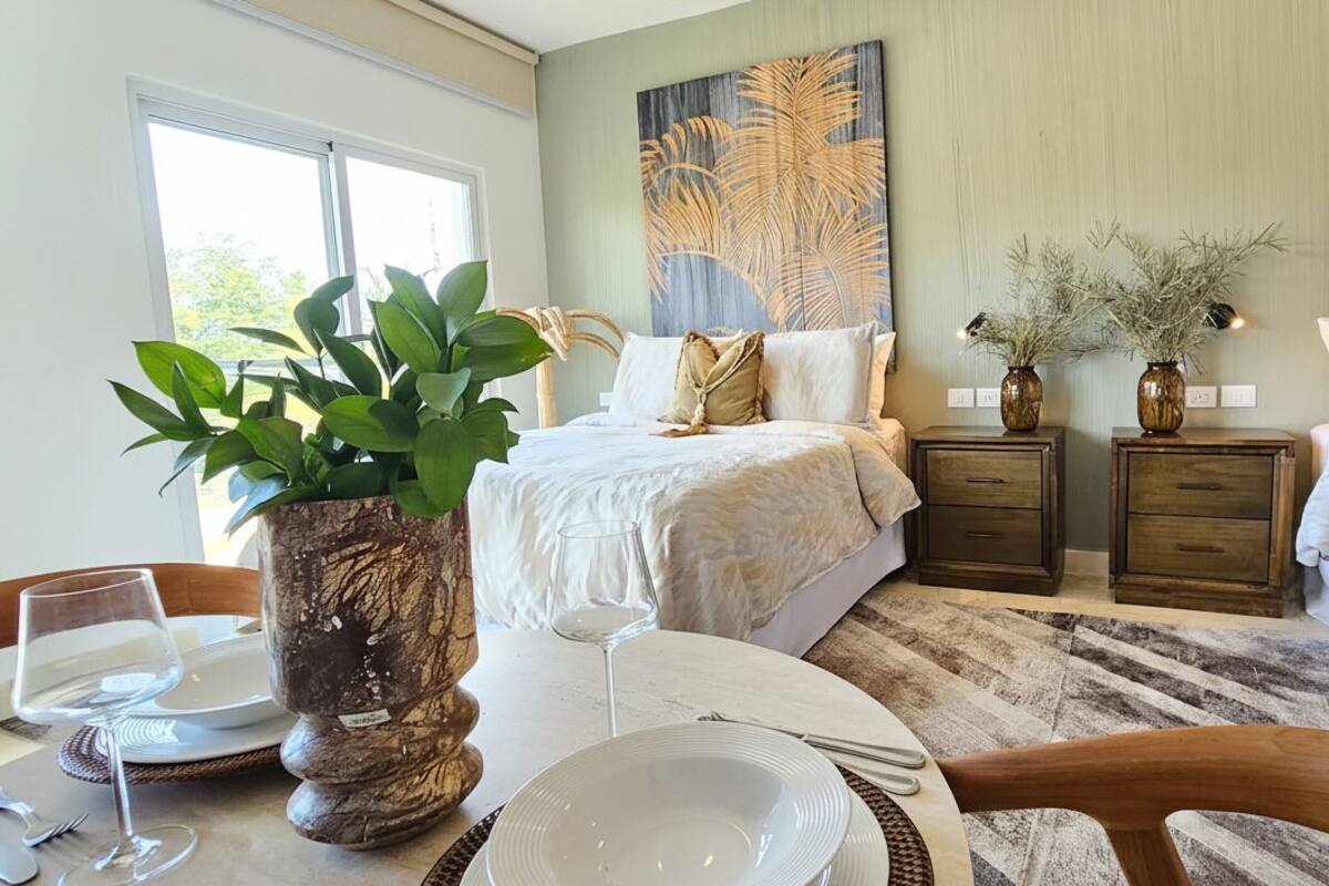 A hotel room with two beds, a dining table with plates and cutlery, a large plant, and artwork on the walls.