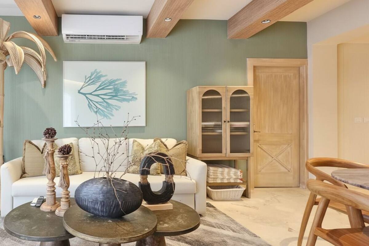 A living room with a sofa, two round tables, a large decorative vase, a wall-mounted air conditioner, and a wooden cabinet.