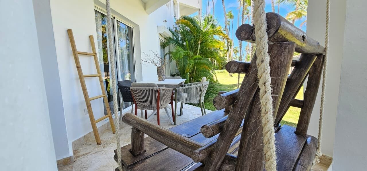 Une terrasse en bois avec une balançoire suspendue à une corde, une échelle et du mobilier d’extérieur.