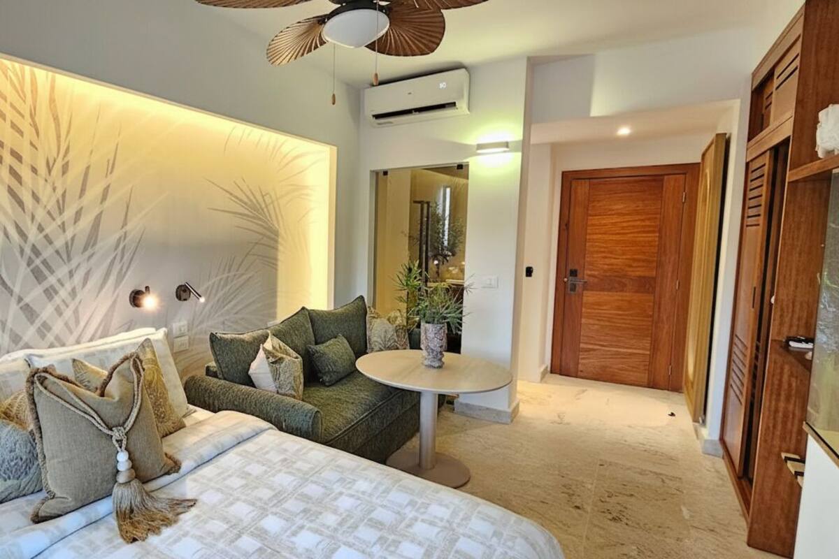 A modern bedroom with a large bed, a sofa, a small table, and a wall with a leaf pattern.