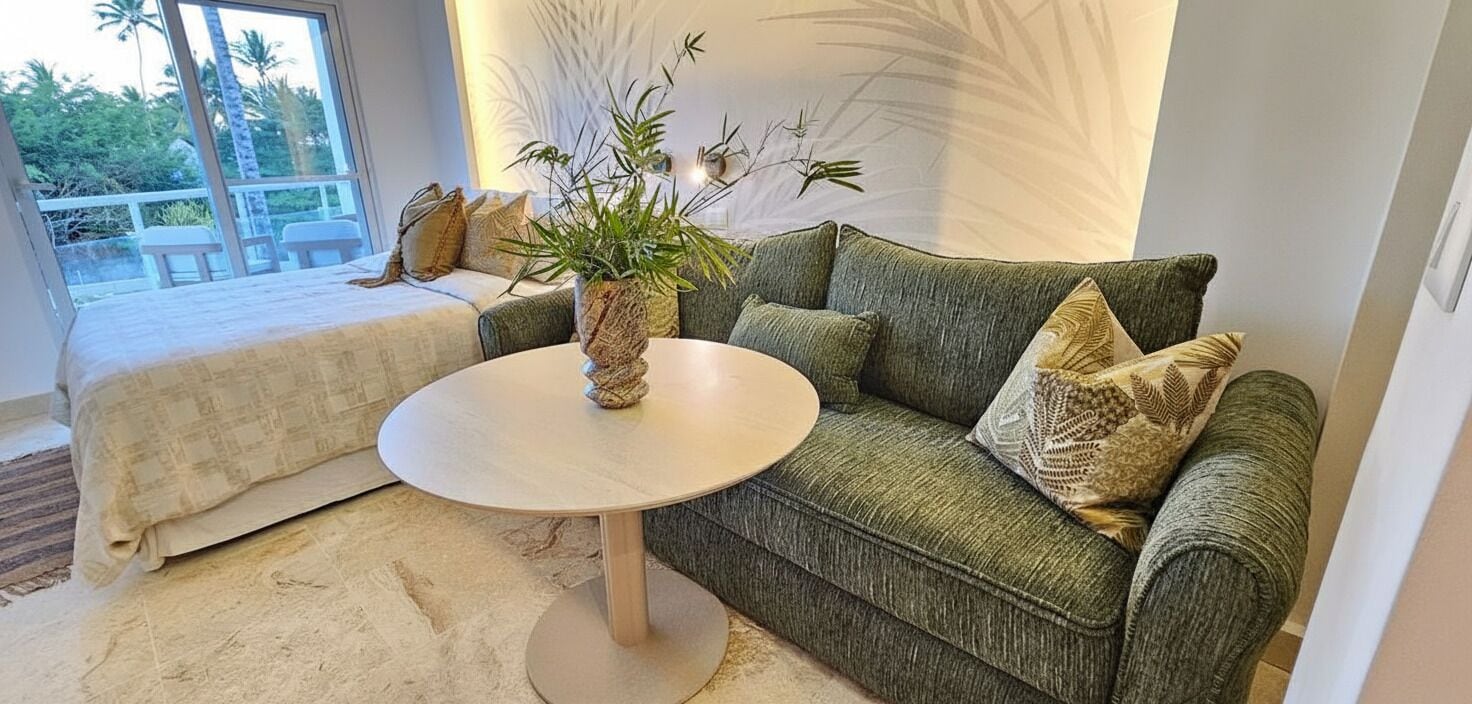 Een kamer met een groene bank, een ronde tafel en een potplant.