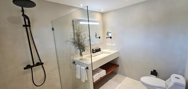 A modern bathroom with a glass shower enclosure, a white sink, a mirror, and a toilet. - MŪTE AT COSON BAY HOTEL AND RESIDENCES (Las Terrenas)