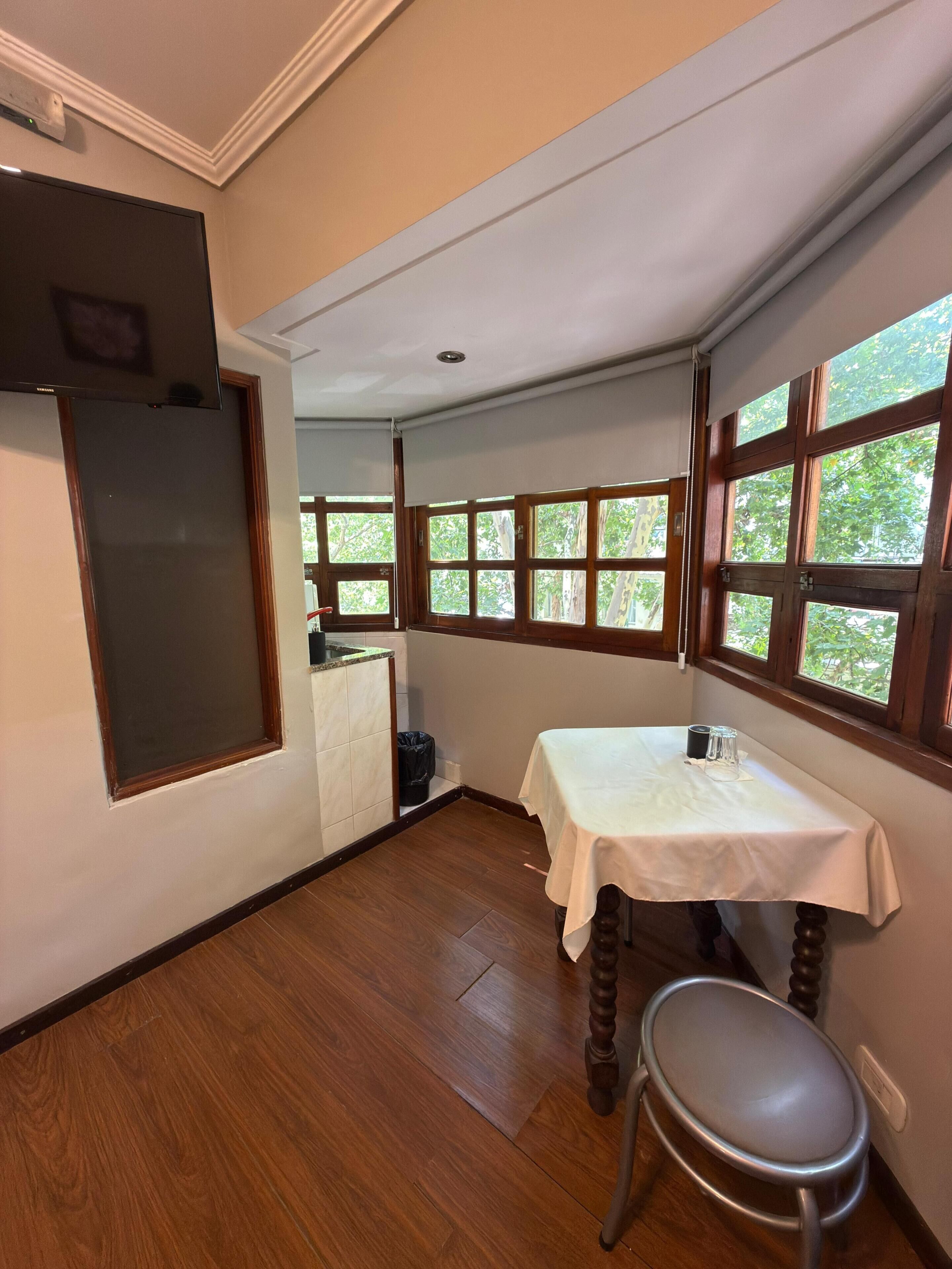 Una habitación con una mesa, una silla y ventanas amplias con vistas a árboles.