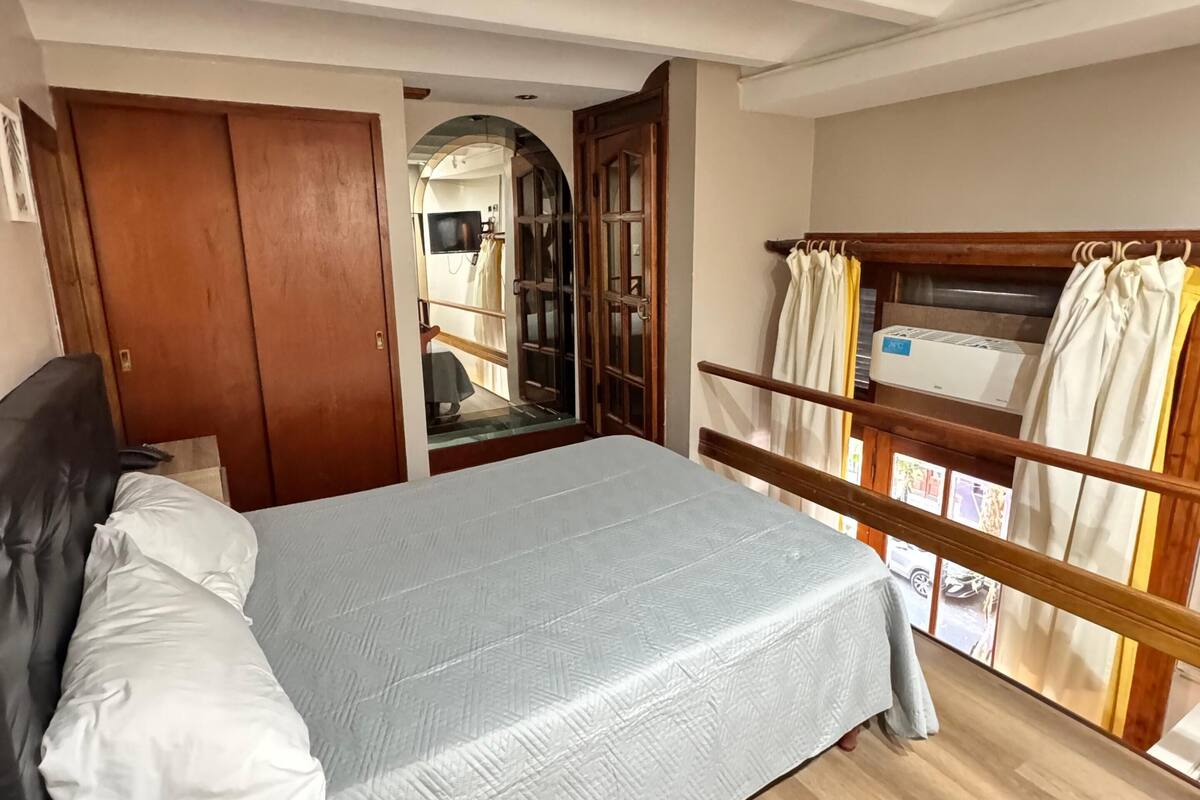 Une chambre à coucher avec un lit, une tête de lit en bois, une armoire, un plancher en bois et un balcon avec des rideaux.