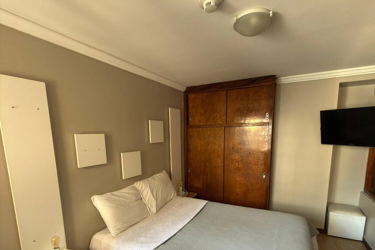 Une chambre à coucher comprenant un lit, une armoire, un téléviseur et une table de chevet avec une lampe.