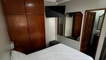 Un dormitorio con cama, armario, espejo y lámpara en el techo.