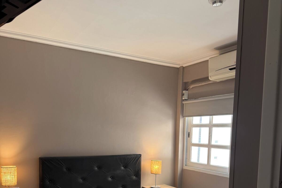 Une chambre à coucher comprenant un lit, deux tables de chevet, une fenêtre et un appareil de climatisation.