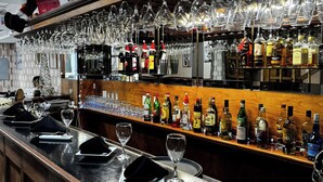 Una zona de bar con una barra alargada, varios vasos de vino colgados encima y una variedad de botellas de licor.