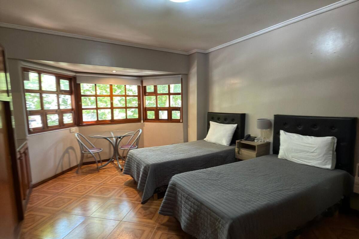 Une chambre avec deux lits, une chaise, une petite table et une fenêtre donnant sur un paysage verdoyant.