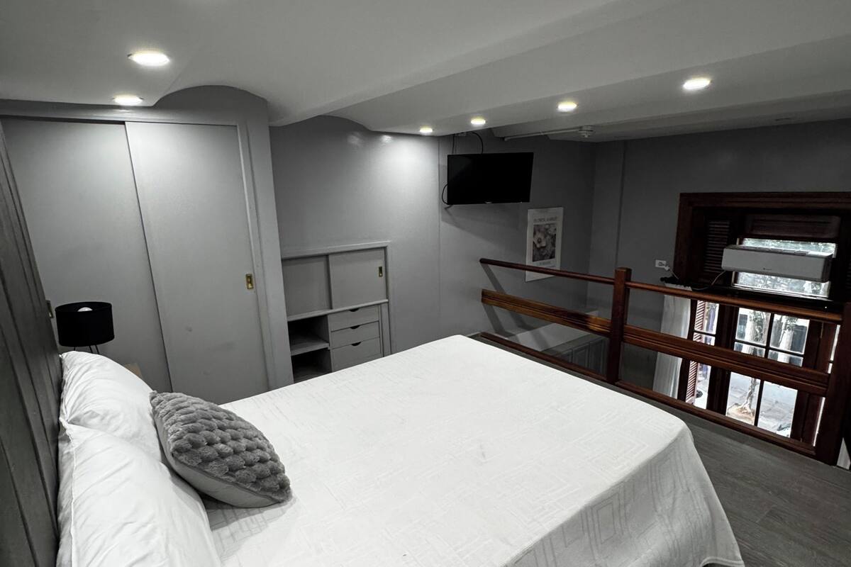Une chambre à coucher avec un lit, un téléviseur fixé au mur, un bureau et une fenêtre donnant sur un beau paysage.