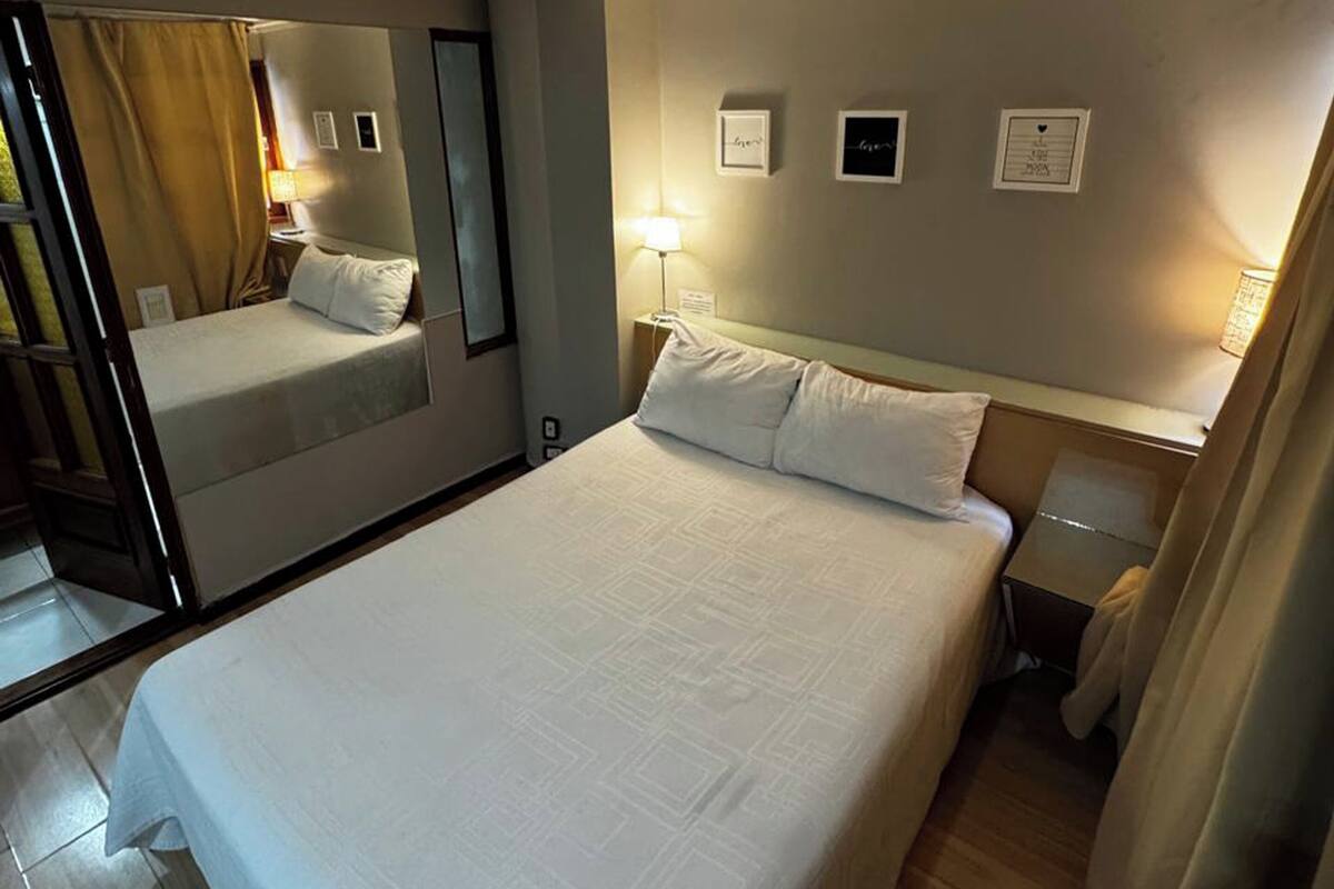 Une chambre d’hôtel avec un grand lit, une table de chevet avec une lampe, un miroir et un mur orné de tableaux.
