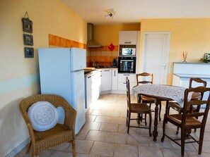 Una cocina funcional con refrigerador, horno y microondas. Cuenta con una mesa de comedor con sillas y una silla de mimbre con cojín.