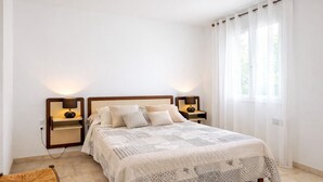 Een netjes opgemaakt slaapkamer met een bed, twee nachtkastjes met lampen, een stoel en een raam met gordijnen.
