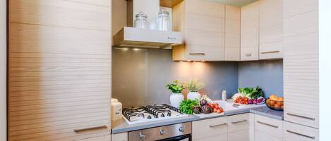 Una cocina moderna con armarios de madera, estufa a gas, horno y una encimera con verduras frescas y frascos.