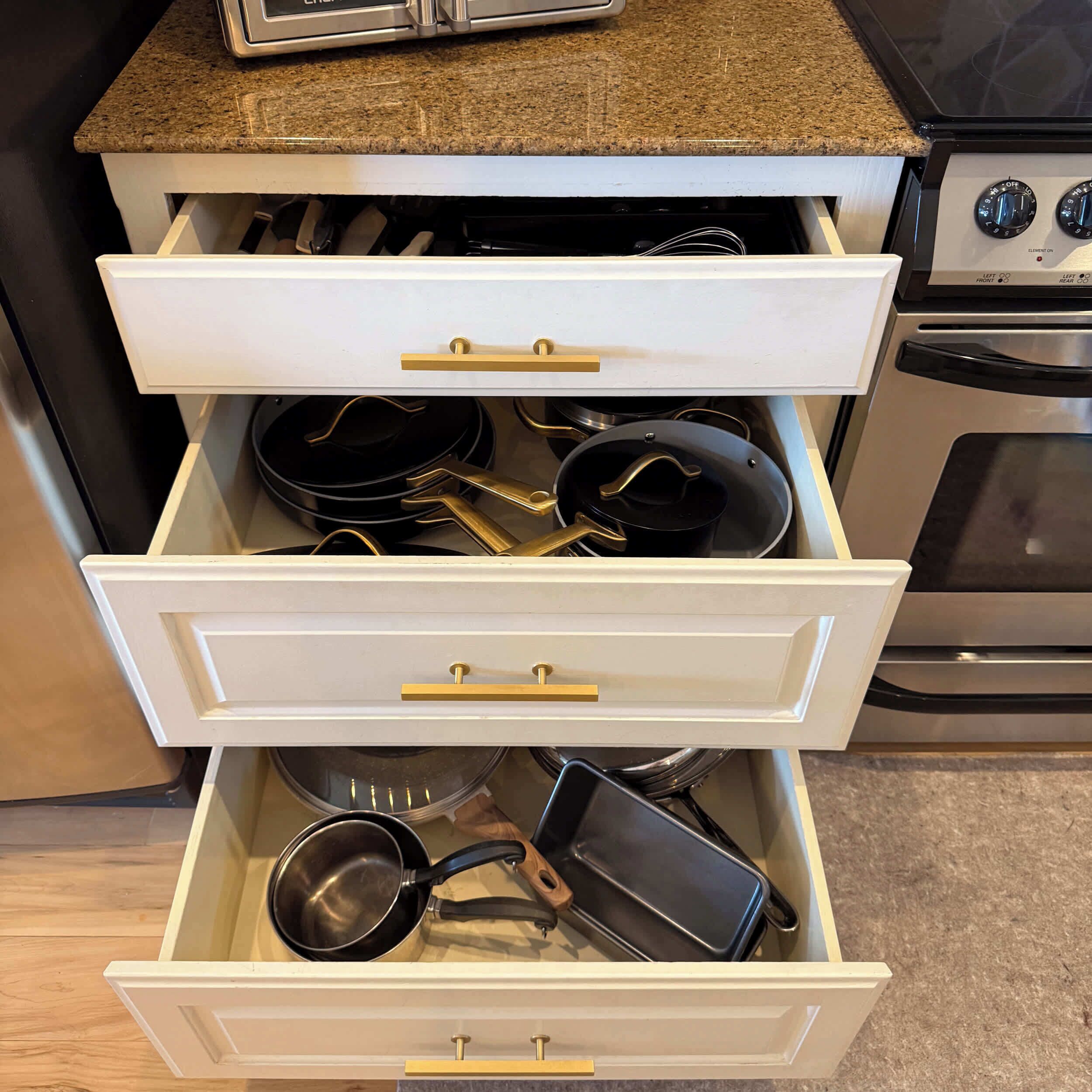 A kitchen drawer with multiple compartments, containing various kitchen utensils and cookware.