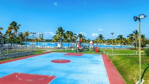 A basketball court with a blue and red surface, surrounded by a fence, palm trees, and a clear sky. - Playa Blanca Signature (Rio Hato)