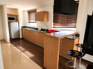 A modern kitchen with wooden cabinets, a stainless steel refrigerator, a microwave, and a coffee maker.
