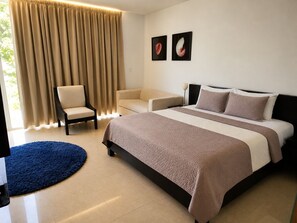 A hotel room with a bed, two chairs, a blue rug, and curtains.