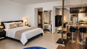 A modern hotel room with a large bed, a separate bathroom, a dining area with bar stools, and a TV. - Playa Blanca Signature (Rio Hato)