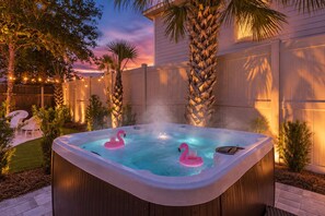A hot tub with two pink flamingos, surrounded by palm trees and a wooden fence. - Heated Pool, Hot Tub & Fire Pit | Walk to Beach (Destin)
