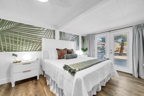 Ein Schlafzimmer mit Bett, Nachttischen, einem Spiegel, einem Fenster mit Vorhängen und Blick ins Freie.