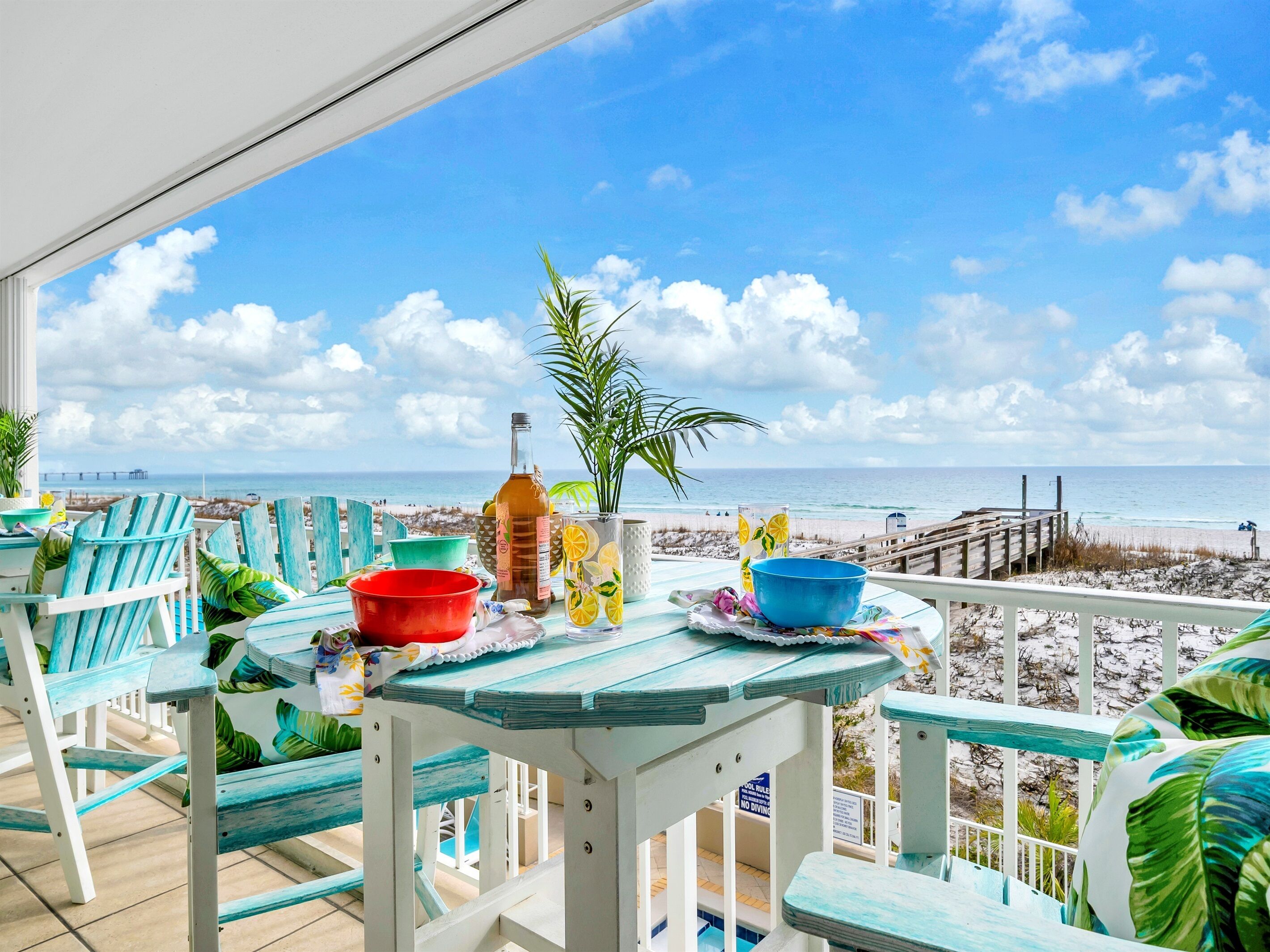 Un balcon avec vue sur la plage, une table avec une bouteille, des verres et un saladier.