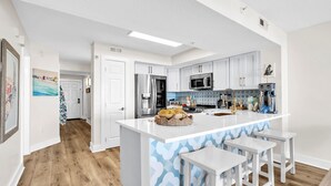 Ett modernt kök med vita skåp, en köksö med barstolar, rostfria vitvaror och ett mönstrat stänkskydd.