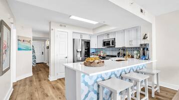 Une cuisine moderne avec des meubles blancs, un îlot central doté de tabourets, des appareils en acier inoxydable et un pare-feu décoratif.