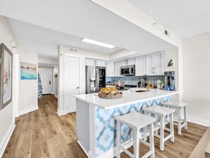 Une cuisine moderne avec des meubles blancs, un îlot central doté de tabourets, des appareils en acier inoxydable et un pare-feu décoratif.
