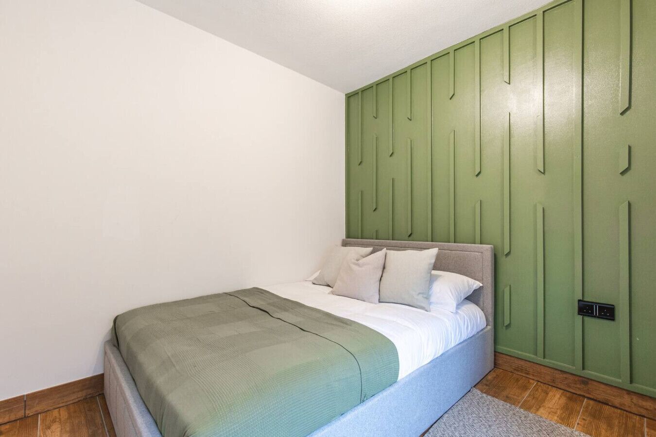 A bedroom with a bed, a green headboard, and a white wall.