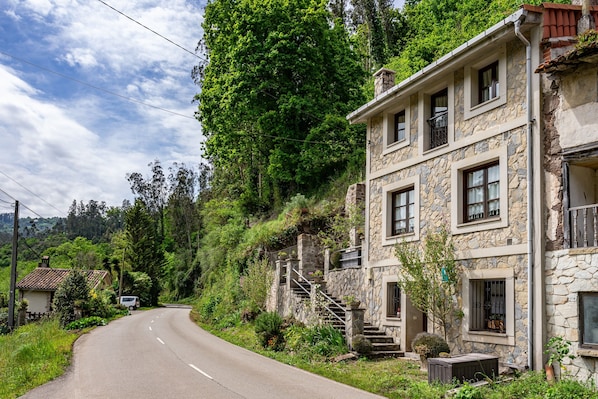 A stone building with a staircase, a road, and greenery.