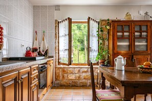 Una cocina con paredes de piedra, armarios de madera, una ventana con cortinas y una mesa de comedor con sillas.