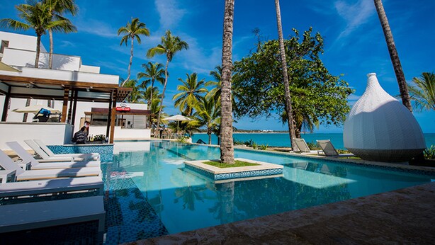 Un área de piscina con sillas de descanso, palmeras y un edificio moderno con una estructura en forma de cúpula blanca.