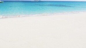 Una playa con aguas turquesas cristalinas, una orilla de arena blanca y una isla distante.