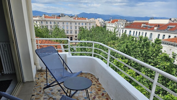Ein Balkon mit zwei Stühlen, einem Tisch, einem Fliesenboden und einem weißen Geländer.