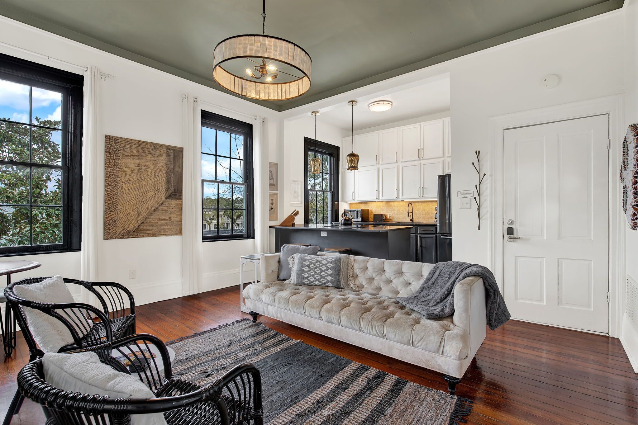 A modern living room with a sofa, chairs, a rug, and a kitchen area with cabinets and a countertop.