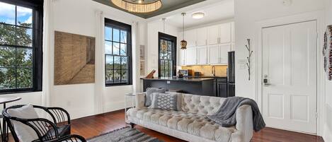 A modern living room with a sofa, chairs, a rug, and a kitchen area with cabinets and a countertop.