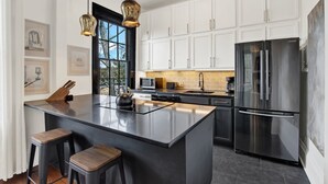 A modern kitchen with white cabinets, a large stainless steel refrigerator, a central island with stools, and pendant lighting. - The Treehouse Walk to Forsyth, Balcony (Savannah)