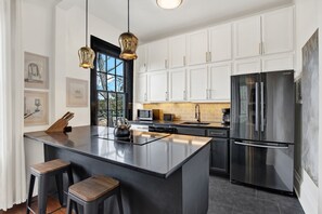 A modern kitchen with white cabinets, a large stainless steel refrigerator, a central island with stools, and pendant lighting. - The Treehouse Walk to Forsyth, Balcony (Savannah)