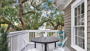 A covered outdoor area with a round table and chairs, a white railing, and large trees. - The Treehouse Walk to Forsyth, Balcony (Savannah)