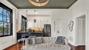 A living room with a tufted sofa, a dining table, and a kitchen in the background. - The Treehouse Walk to Forsyth, Balcony (Savannah)
