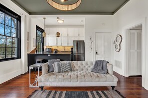 A living room with a tufted sofa, a dining table, and a kitchen in the background. - The Treehouse Walk to Forsyth, Balcony (Savannah)